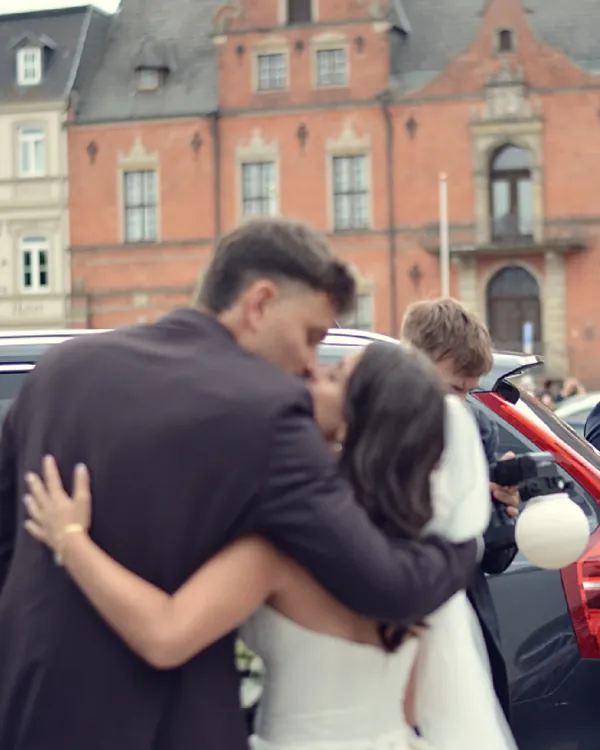 Brautpaar küsst sich vor dem Hochzeitsauto