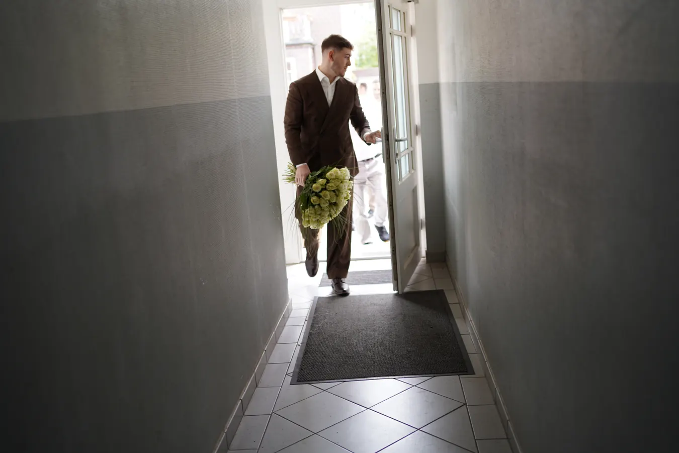 Der Bräutigam betritt mit Blumen das Haus