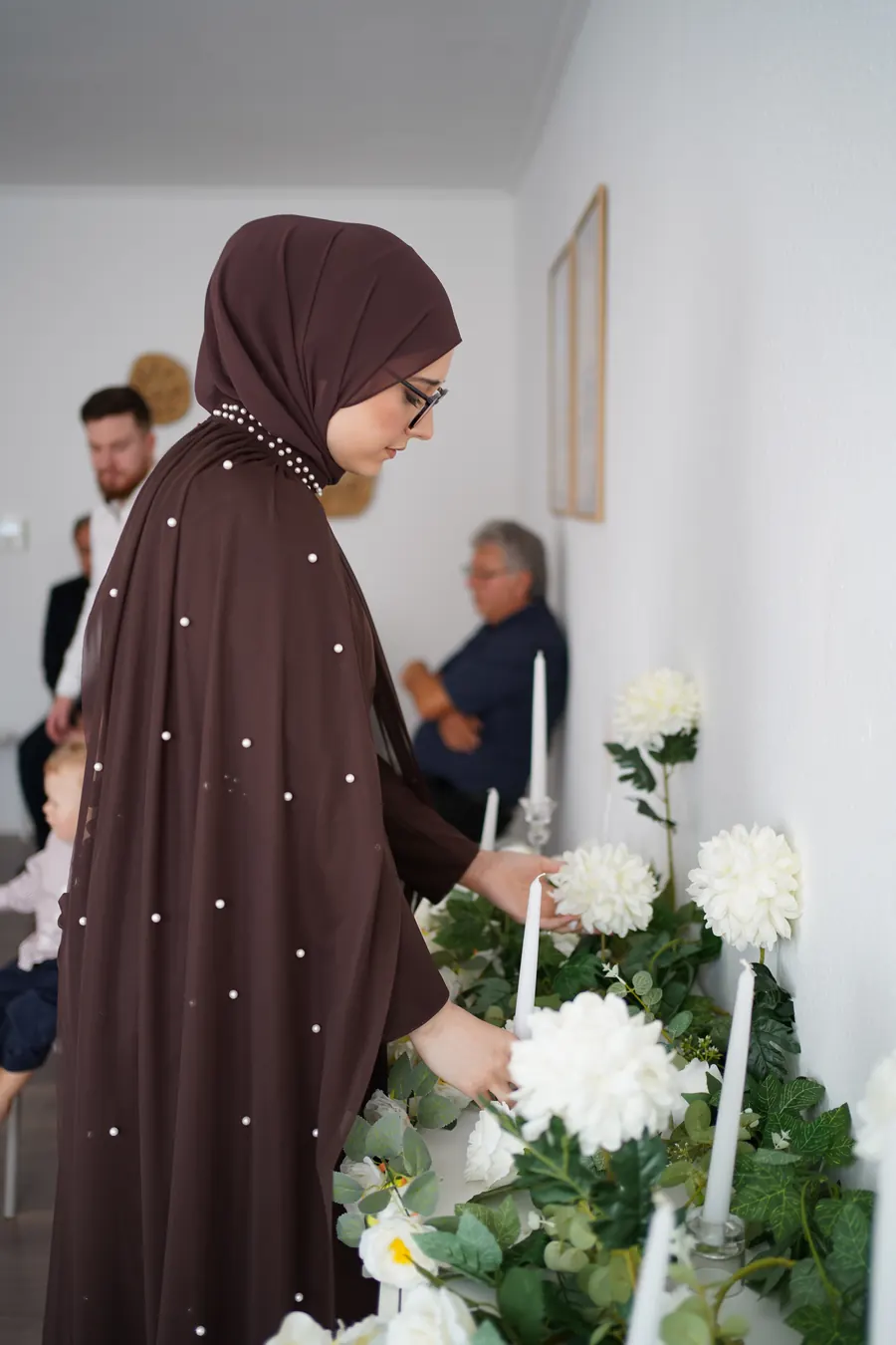 Die Braut zündet Kerzen zwischen weißen Blumen an